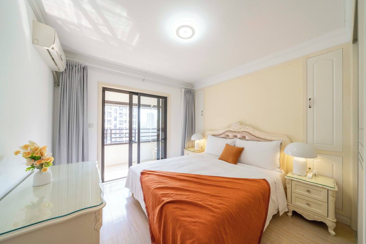 Habitación de hotel con cama, mesita de noche, lámpara y vistas al exterior.