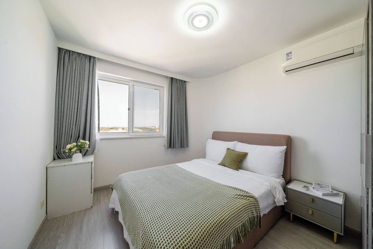 Un dormitorio con cama, mesita de noche, ventana y aire acondicionado.