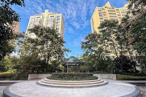 Una plaza circular con un pabellón central, rodeada de árboles y un seto, con edificios residenciales altos al fondo.