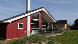 Un bâtiment rouge avec une cheminée blanche, une grande fenêtre en verre et un patio aménagé avec du mobilier d’extérieur.