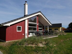 A red building with a white chimney, a large glass window, and a patio area with outdoor furniture. - 4 Star Holiday Home in Grossenbrode (Grossenbrode)