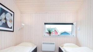 Une chambre avec deux lits, une fenêtre donnant sur des maisons, un radiateur et un tableau encadré au mur.