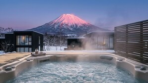 Un jacuzzi con vista a la montaña, edificios modernos y una terraza de madera.