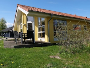 Ein gelbes Gebäude mit rotem Ziegeldach, einer überdachten Terrasse mit Tisch und Stühlen und einem kleinen Garten.