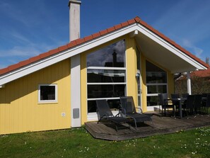 Ein gelbes Gebäude mit rotem Dach, großen Fenstern und einer Terrasse mit Sitzgelegenheiten.
