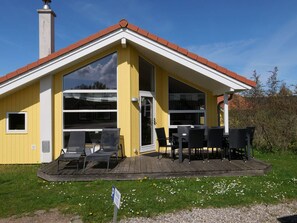 Ein gelbes Gebäude mit rotem Dach, großen Fenstern und Außenbereich zum Sitzen.