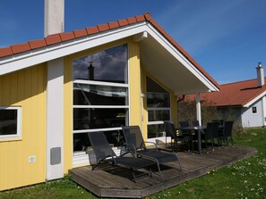 A yellow building with large windows, a deck with chairs, and a red-tiled roof. - 4 Star Holiday Home in Grossenbrode (Grossenbrode)