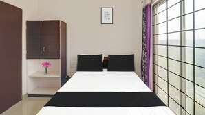 Una camera da letto con un letto, un armadio, un piccolo ripiano con fiori, un quadro appeso al muro e una finestra vista.