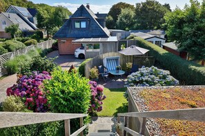 A residential property with a sloped roof, a fenced garden, and a patio area with outdoor furniture. - Beach thistle - Westerland (Westerland)