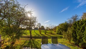 Ein Sitzbereich im Freien mit Tisch und Stühlen, umgeben von Bäumen und einer Wiese.