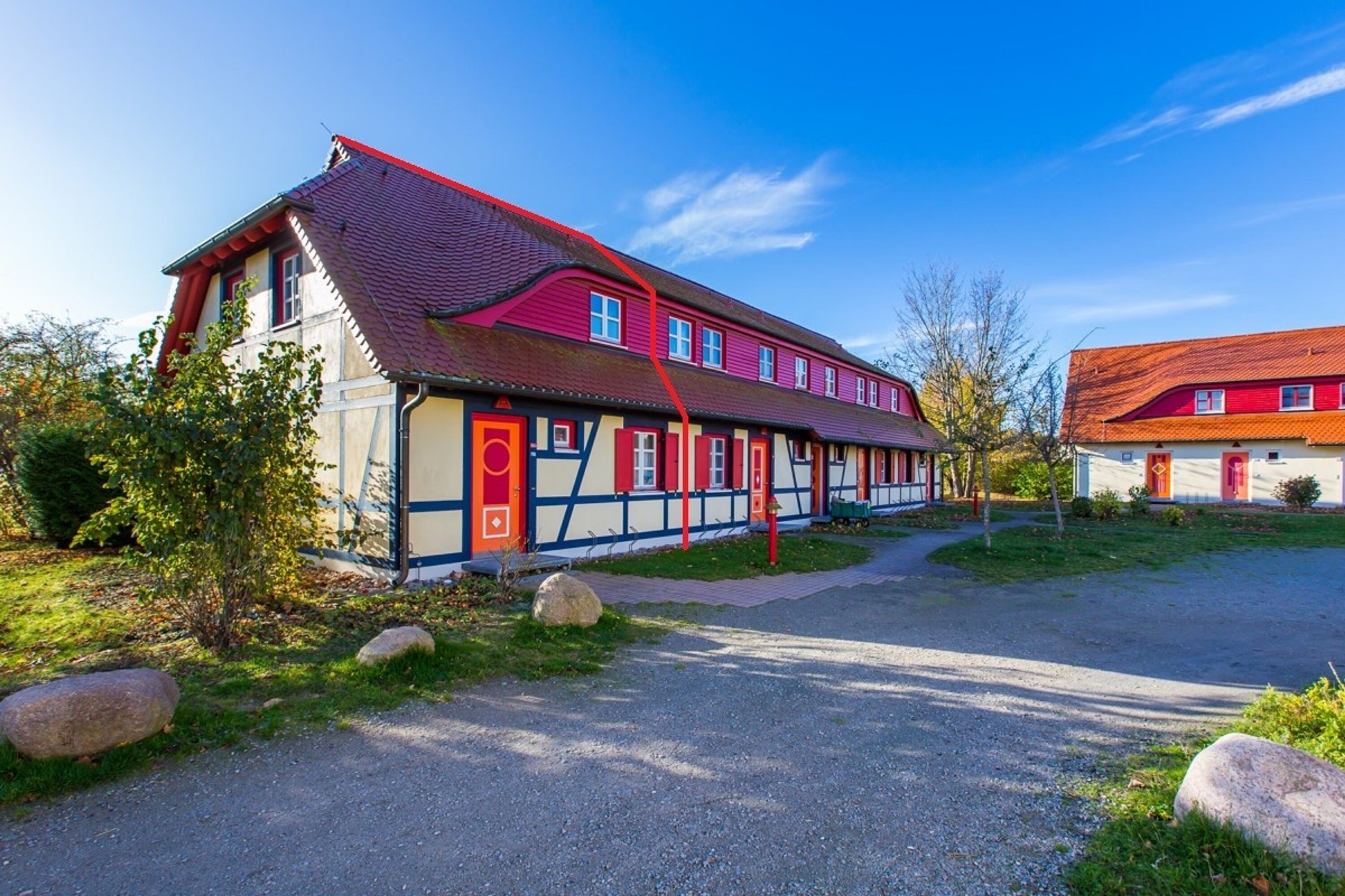 A traditional building with a red roof, multiple windows, and a gravel driveway.
