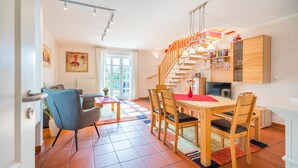 Eine moderne Küche mit Holzausstattung, ein Essbereich mit Holztisch und -stühlen, eine Treppe und ein Wohnzimmer mit Sofa und Couchtisch.
