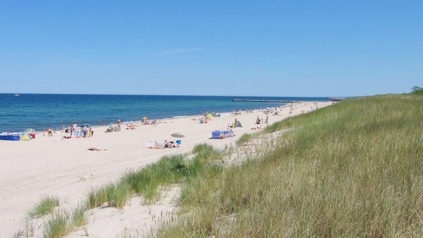 Ein Strand mit Sand, Gras und dem Meer.