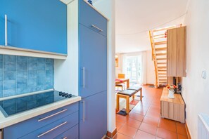 A compact kitchen with blue cabinets, a gas stove, and a dining area with a wooden table and chairs. - Vacation apartment close to the beach with its own terrace - Feriendorf Bakenberg FeWo B66 (Dranske)