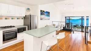 A modern kitchen with a central island, white cabinetry, stainless steel appliances, and a view to the outside. - Panorama 3 & Free Buggy - Hamilton Island (Hamilton island)