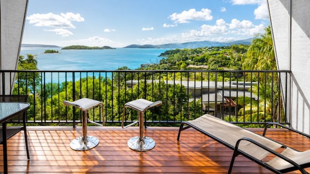 A balcony with a wooden floor, two tables, and a bench. - Panorama 3 & Free Buggy - Hamilton Island (Hamilton island)