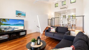 A modern living room with a flat-screen TV, dark sofas, a coffee table, and a staircase leading to an upper level. - Panorama 3 & Free Buggy - Hamilton Island (Hamilton island)