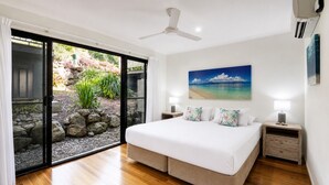 A bedroom with a bed, a nightstand, a ceiling fan, and a view of a garden through a sliding glass door. - Panorama 3 & Free Buggy - Hamilton Island (Hamilton island)