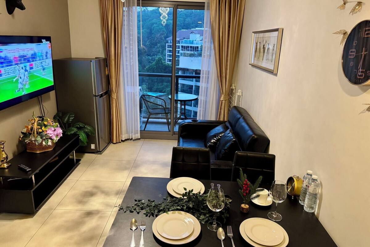 A living room with a TV, a sofa, a dining table set for two, and a balcony with a view.