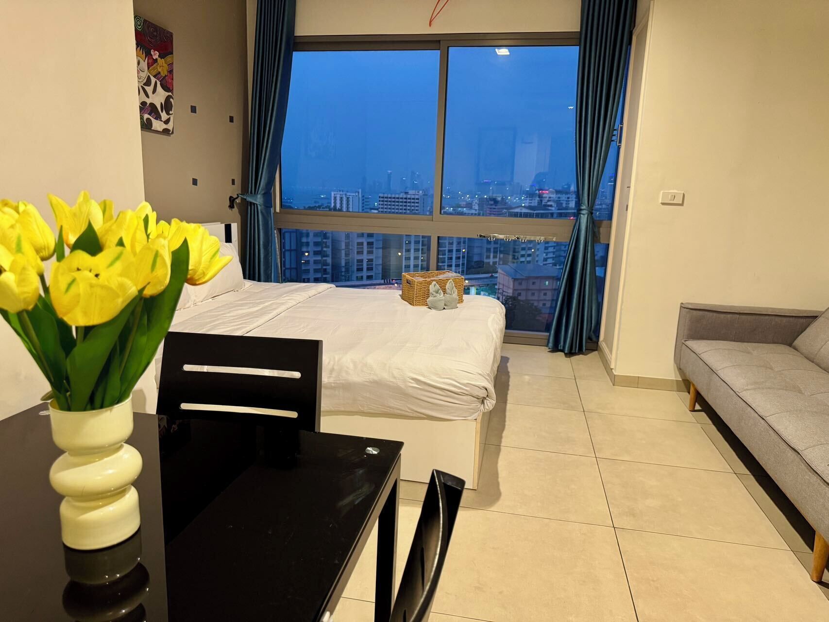 A modern hotel room with a large window, a bed, a dining table, and a sofa.