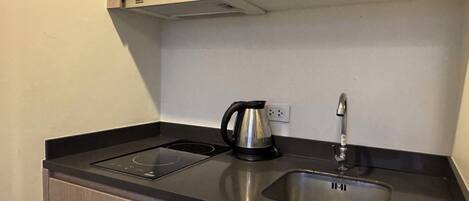 A compact kitchen with a black induction cooktop, a stainless steel sink, and a kettle.