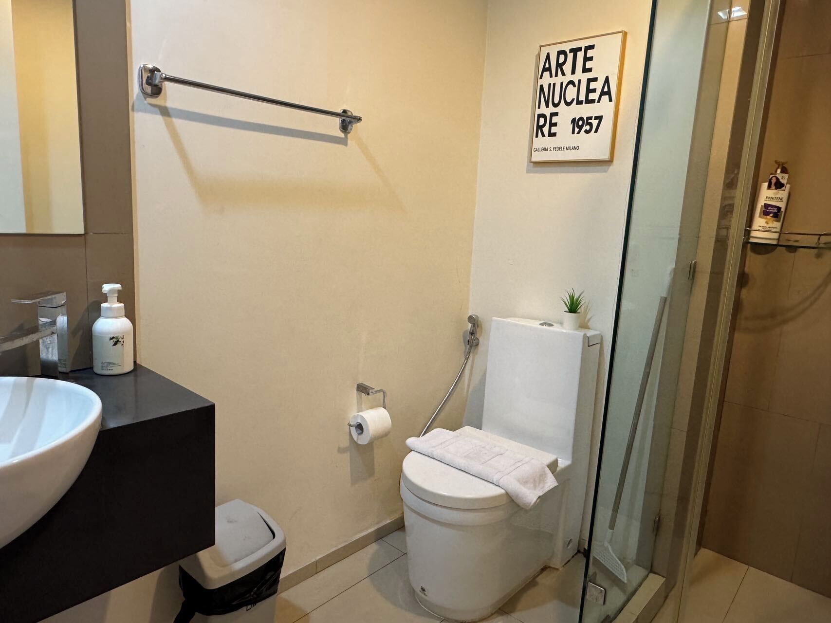 A bathroom with a sink, toilet, shower, and a framed artwork on the wall.