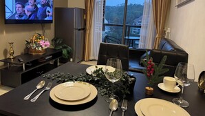 A dining area with a TV, a refrigerator, a sofa, and a table set for two with plates, cutlery, and a glass of wine. - Unixx South Pattaya Condominium (Pattaya)