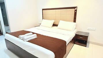 A neatly made bed with a brown headboard, white linens, and a folded towel on the footboard.