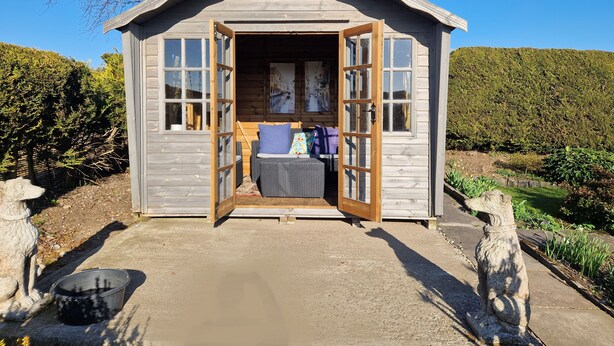 A small wooden cabin with an open door, a bench inside, and a stone statue outside. - 2 Newmill (Stanley)