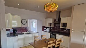 A modern kitchen with white cabinets, a wooden dining table, and a unique stained glass pendant light. - 2 Newmill (Stanley)