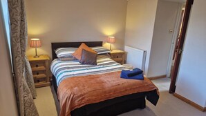 A bedroom with a bed, bedside lamps, a nightstand, a radiator, and a door. - 2 Newmill (Stanley)