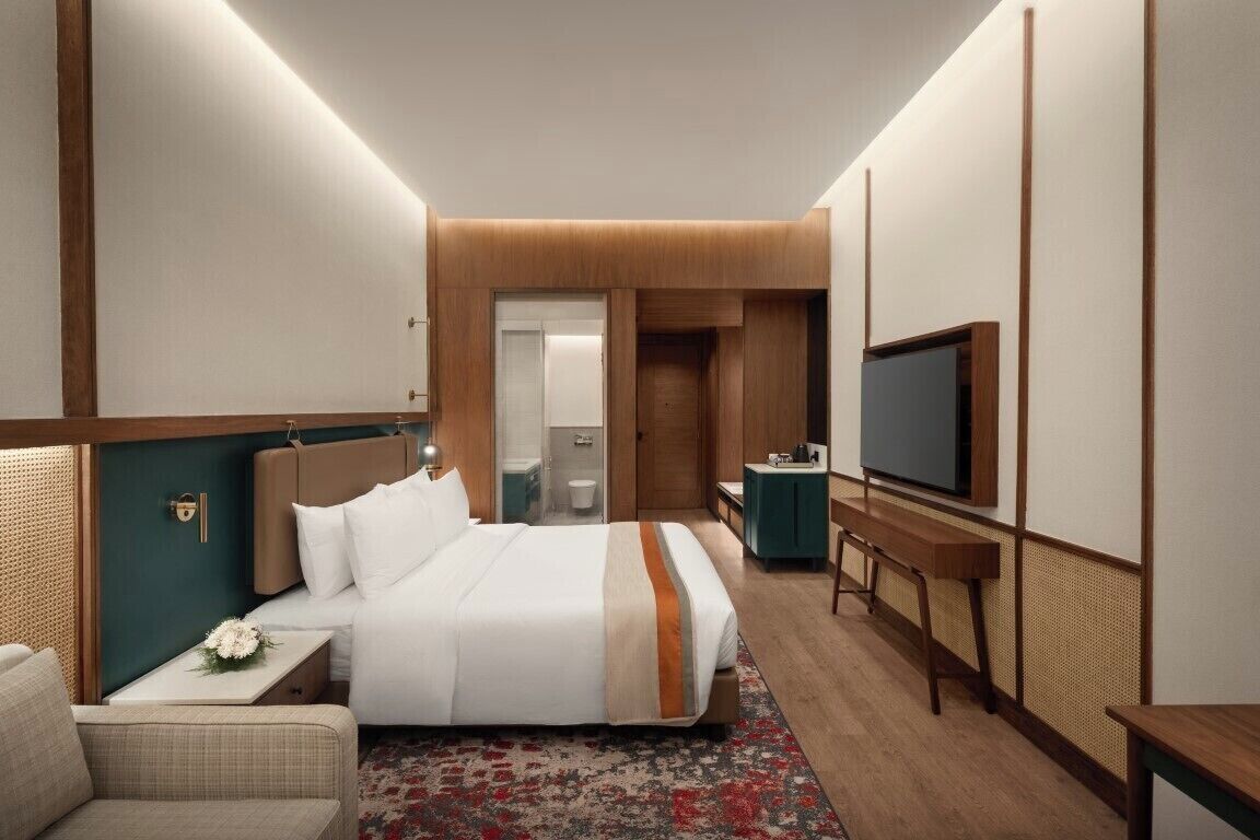 A hotel room with a bed, bedside table, TV, and a bathroom visible through an open door.