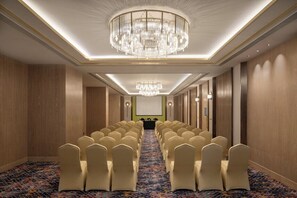 Une salle de conférence avec des rangées de chaises, un écran de projection et un lustre.
