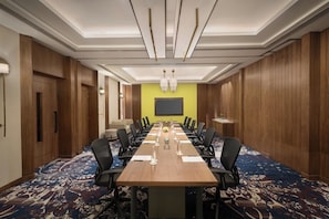 Een vergaderruimte met een lange tafel, stoelen en een projectiescherm.
