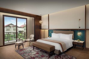 Habitación de hotel moderna con una cama grande, zona de estar y balcón con vistas.