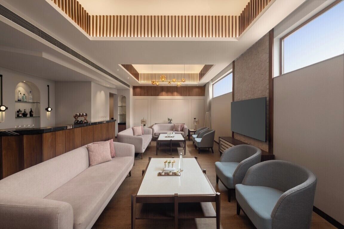 A modern hotel lobby with a sofa, chairs, a coffee table, a TV, and a bar area.