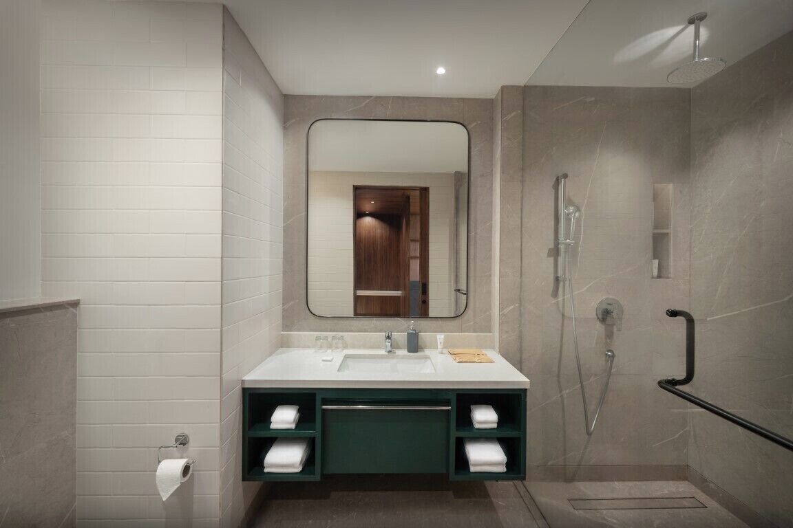 A modern bathroom with a white sink, a mirror, a shower, and a towel rack.