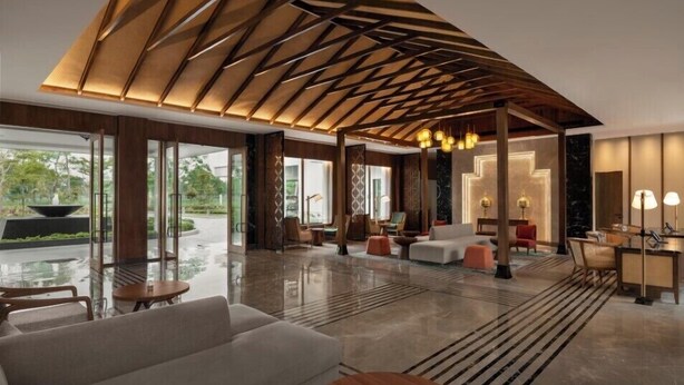 Un interior moderno con una estructura de techo geométrica, una zona de estar con sofás y mesas, y vistas a través de grandes puertas de cristal.