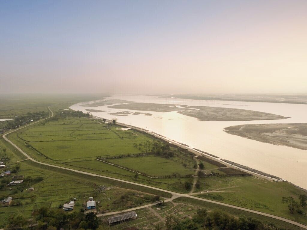 An aerial view of a river with surrounding fields and a few buildings.