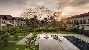 Un patio de hotel con piscina, abundante vegetación y varios edificios con tejados rojos.