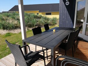 Eine Holzterrasse mit Tisch und Stühlen, eine Glastür mit einer Nummer und ein Gebäude im Hintergrund.