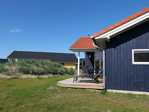 Ein Haus mit dunkler Fassade, rotem Dach und einer Veranda mit Gartenmöbeln.