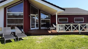 Una casa con un amplio ventanal, una terraza con sillas y una barandilla blanca.