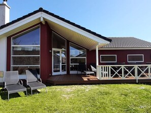 A house with a large glass door, a deck with chairs, and a white railing. - 4 Star Holiday Home in Grossenbrode (Grossenbrode)