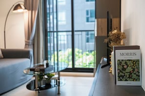 A modern living room with a sofa, a glass coffee table, a lamp, and a book titled 'Morris' by Charlotte & Peter Fell. - 5 Star Sukhumvit 1BR apt Pool, Gym, Sauna Thong lo (Krung Thep Maha Nakhon)