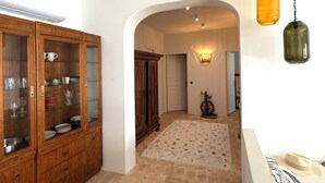 A hallway with a wooden cabinet, a patterned rug, and a wall-mounted light fixture. - Brand-New Villa 'Maison Magnolia', Infinity Pool & Sea View above Skopelos Town (Skopelos)