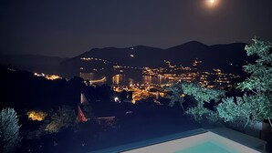 A nighttime view of a coastal town with a pool area in the foreground. - Brand-New Villa 'Maison Magnolia', Infinity Pool & Sea View above Skopelos Town (Skopelos)