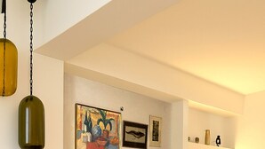 A living room with a sofa, wall art, and a flat-screen TV. - Brand-New Villa 'Maison Magnolia', Infinity Pool & Sea View above Skopelos Town (Skopelos)