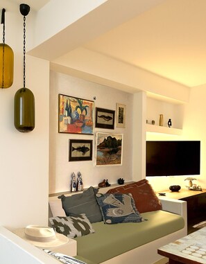 A living room with a sofa, wall art, and a flat-screen TV. - Brand-New Villa 'Maison Magnolia', Infinity Pool & Sea View above Skopelos Town (Skopelos)