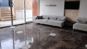 A spacious room with a large sofa, a flat-screen TV mounted on the wall, and a circular ceiling light fixture. - Sarehotel (Kusadasi)